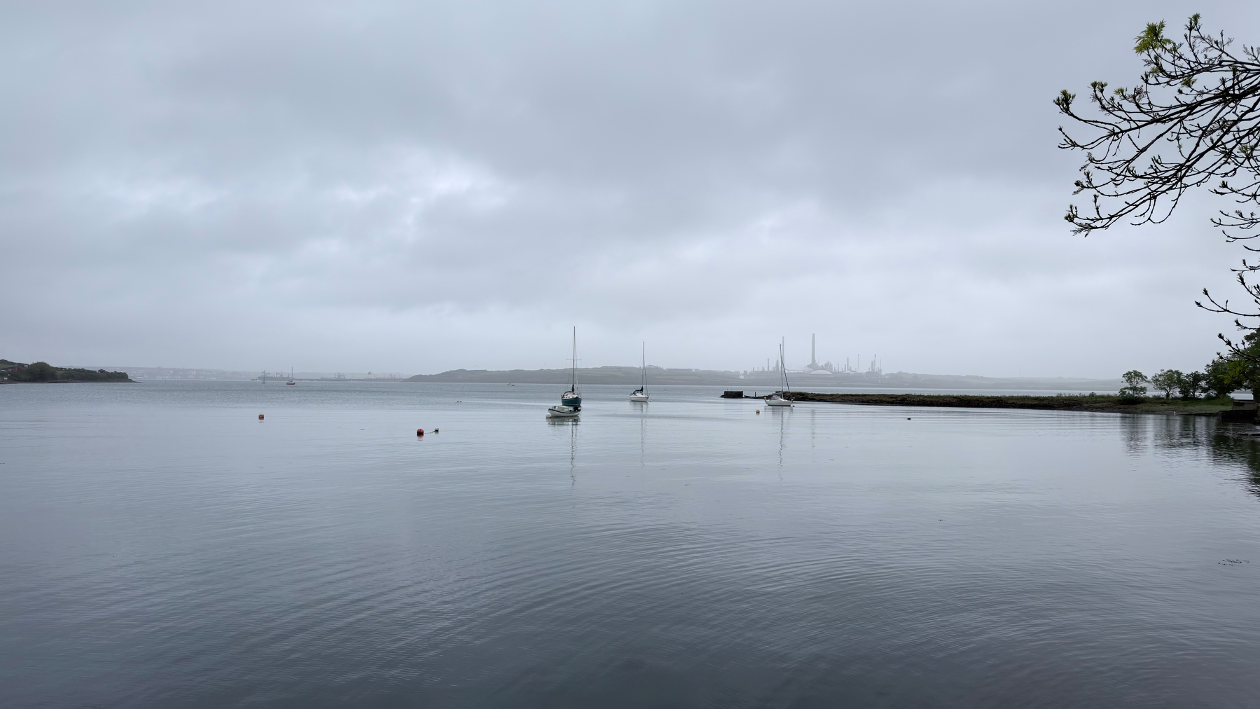 A tranquil seascape features calm waters with a few moored boats and a cloudy sky.