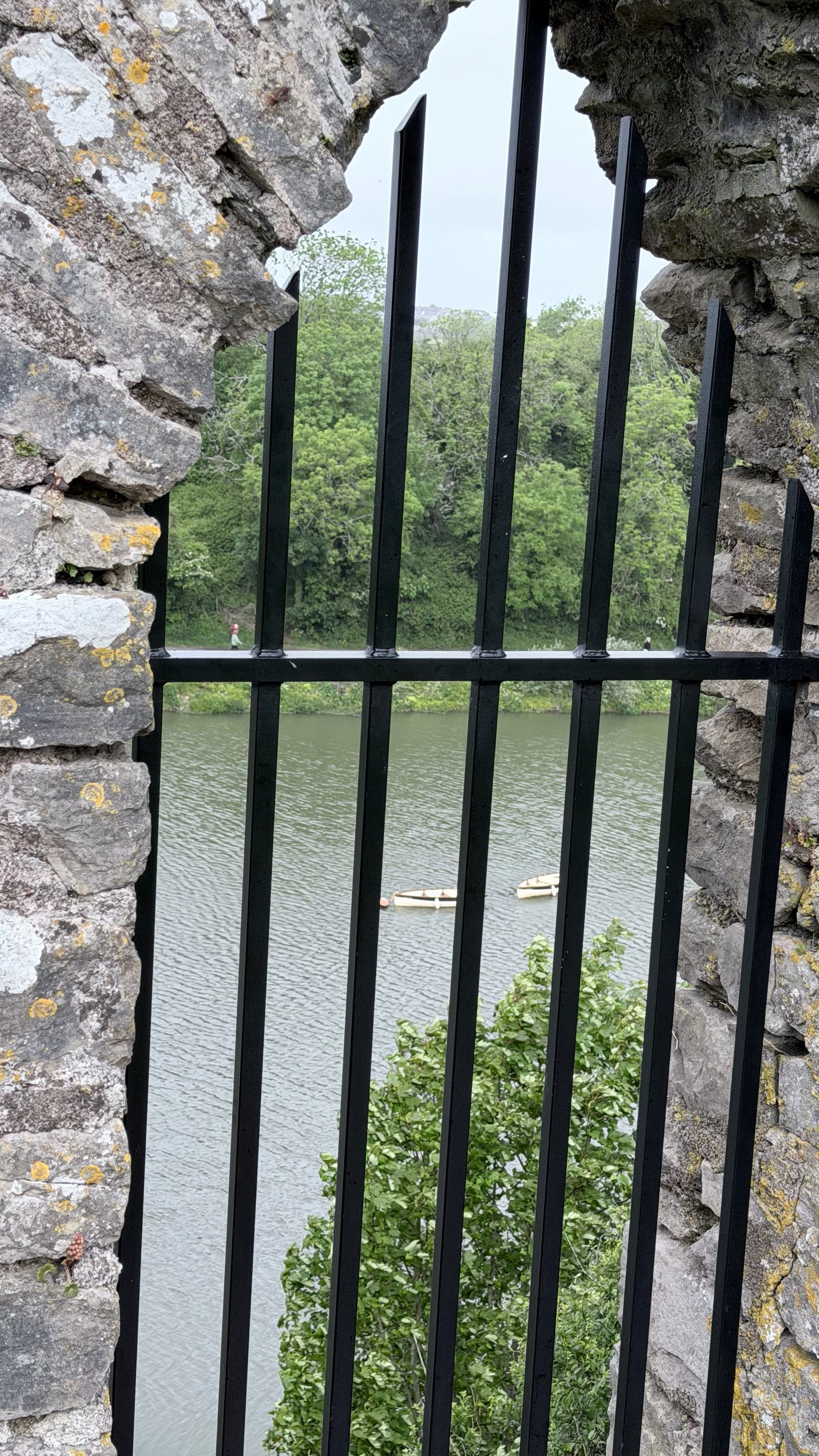 A view of a river and trees is seen through a stone archway barred with metal rods.