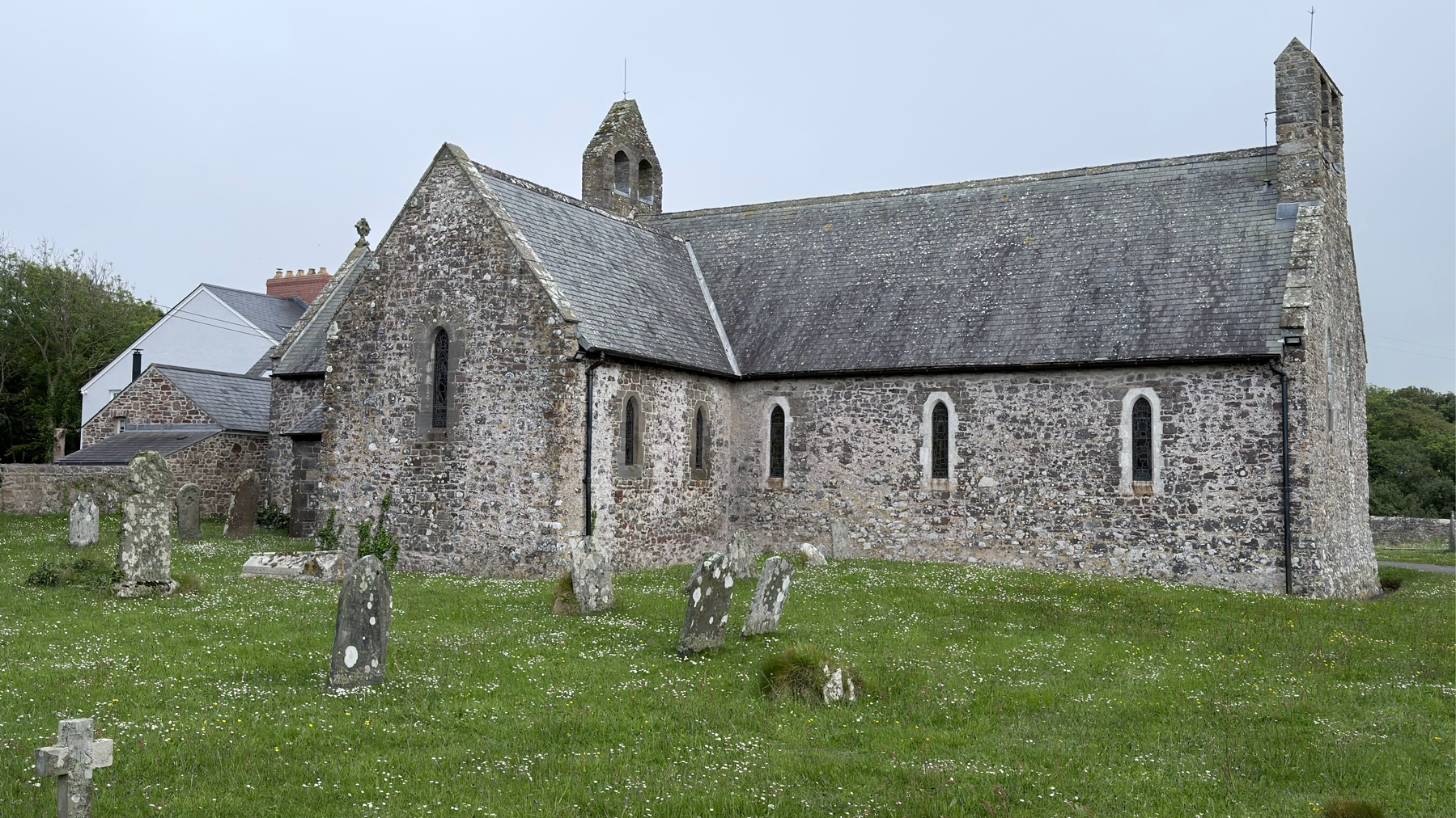 A historic stone church is surrounded by an old graveyard with weathered headstones on a grassy field.
