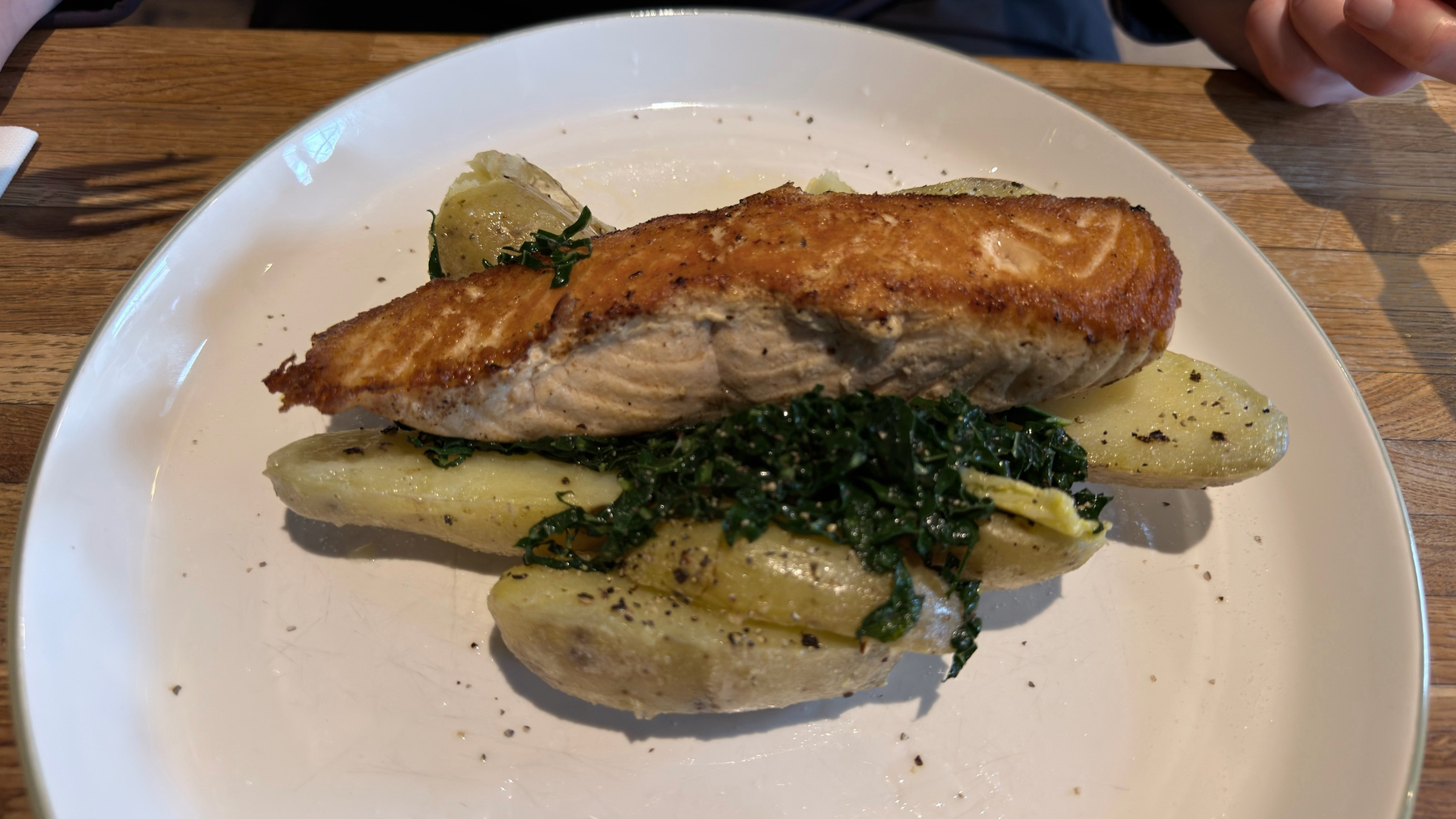 A plate features a piece of grilled salmon atop seasoned potatoes and wilted greens.
