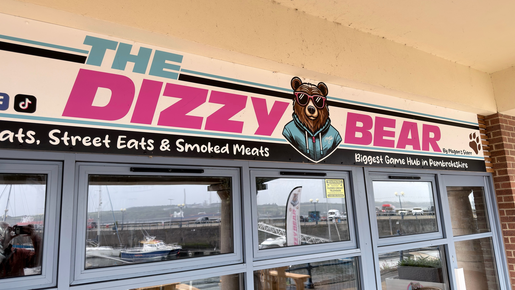 A storefront sign reads THE DIZZY BEAR, depicting a cool bear wearing sunglasses, with text advertising eats, street eats, smoked meats, and a game hub.