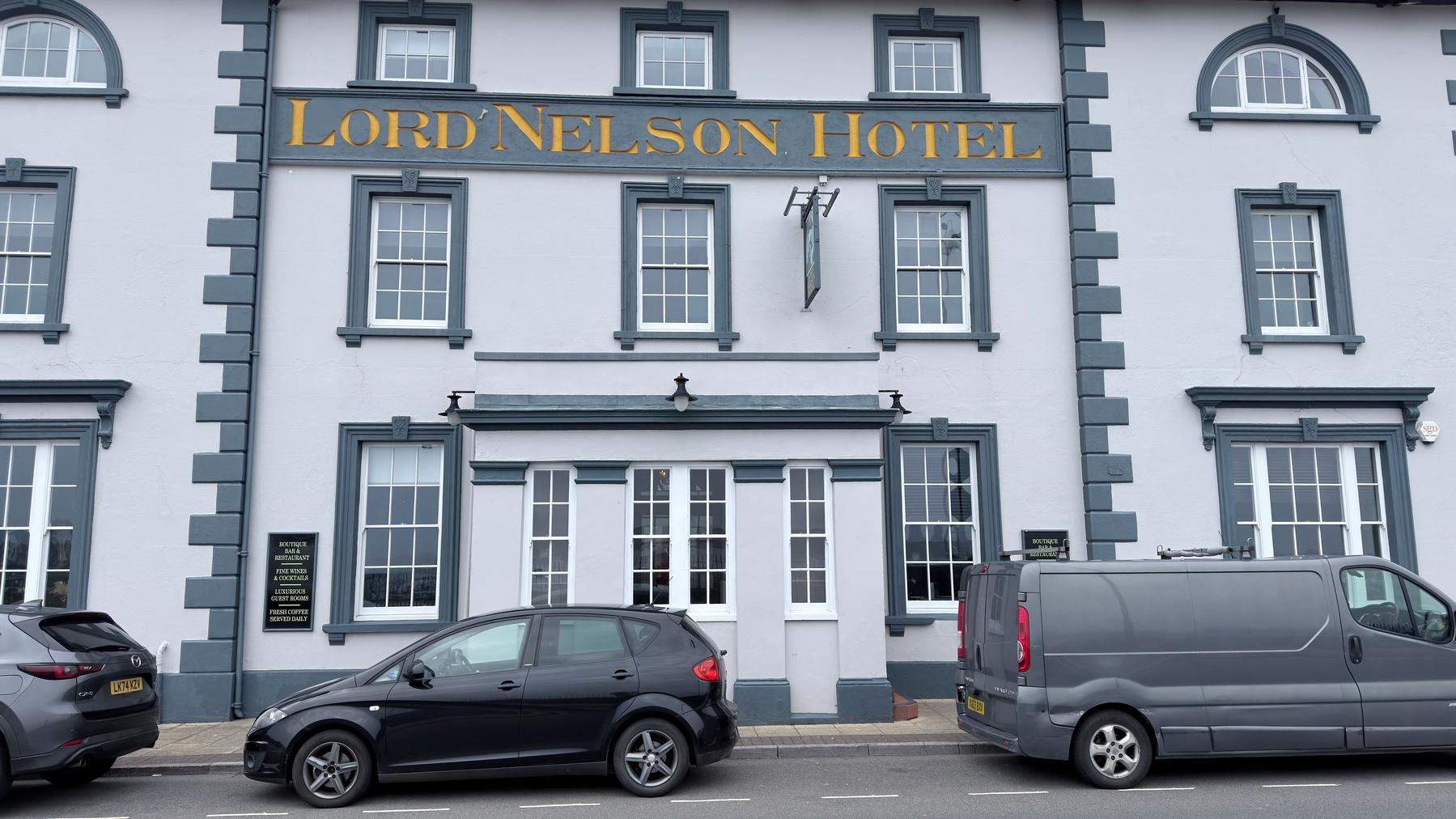 A hotel named Lord Nelson Hotel is shown with multiple windows and a few parked cars in front.